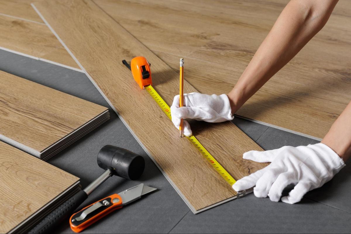 Vinyl plank wordt opgemeten met meetlint en potlood naast hamer en stanleymes.